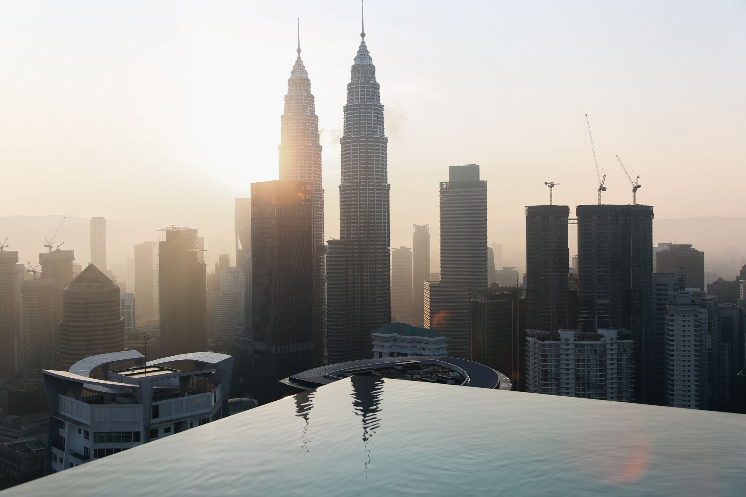 Hazy sunrise over Kuala Lumpur with the Petronas Twin Towers reflected in an infinity pool