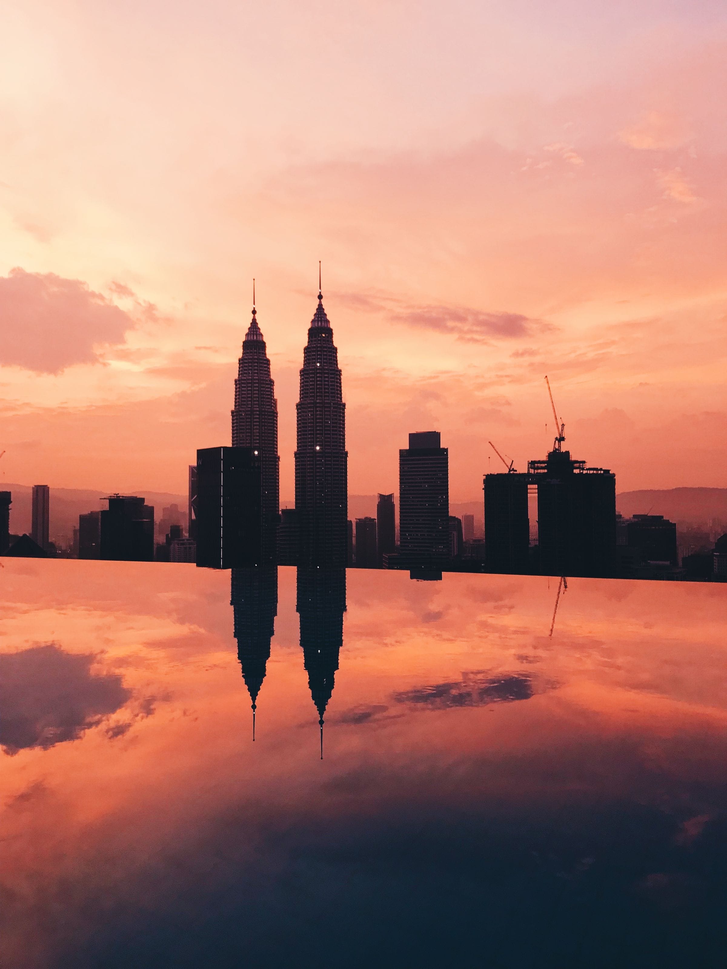 Petronas Twin Towers silhouetted against a pink and orange sunset, reflected in still water